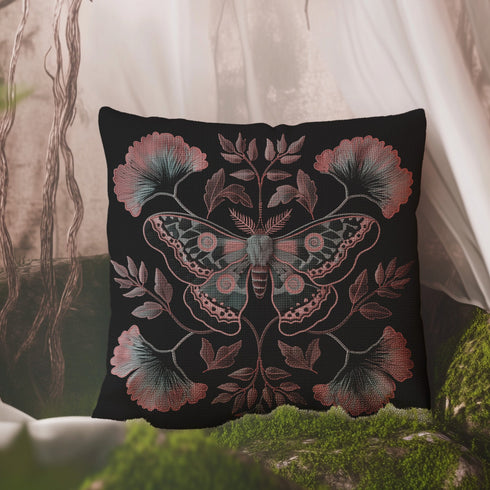 A square decorative pillow featuring an intricately detailed Luna moth in faded rose pink, slate blue and dusty terracotta colors on a black background. The moth is centered in a symmetrical arrangement with ginkgo-inspired leaves and botanical elements surrounding it.